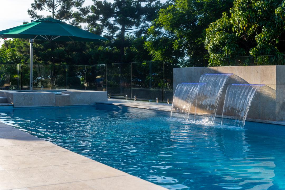 Raised spa and water feature spilling into a fibreglass pool with paved surround