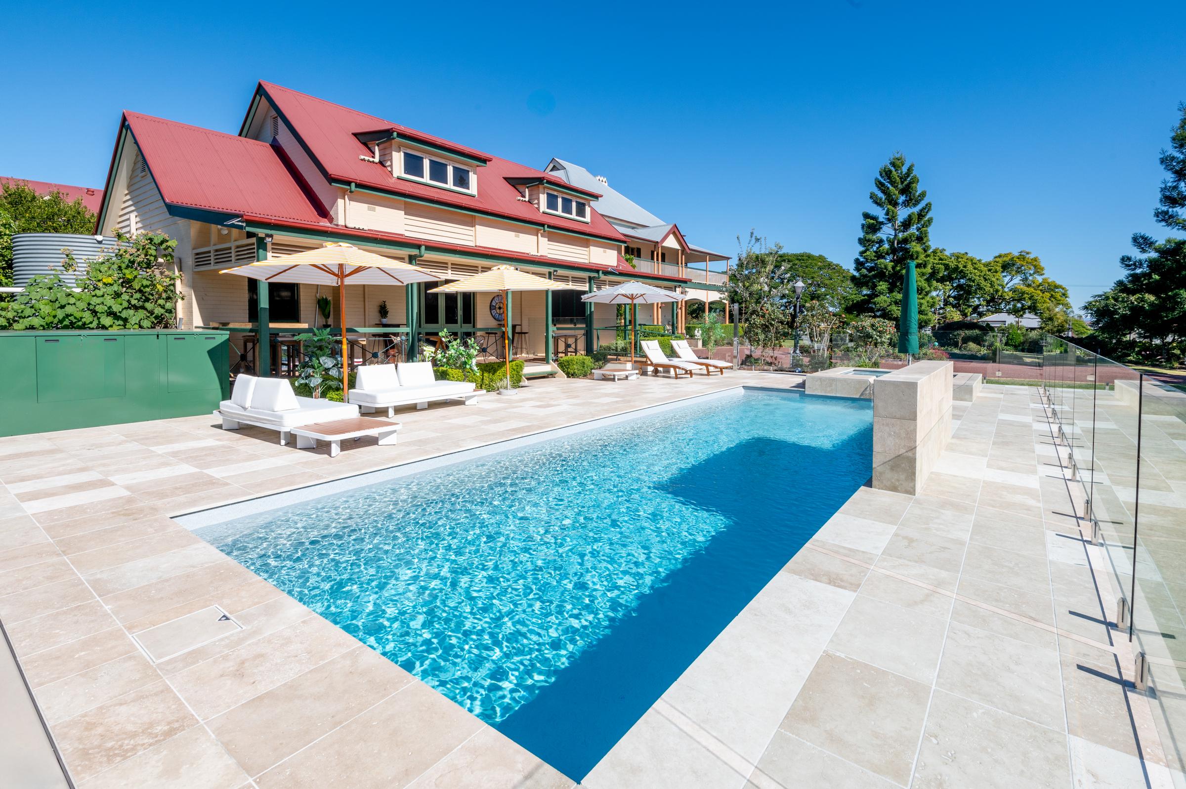 Fibreglass pool with paved surround, glass fencing and a raised spa